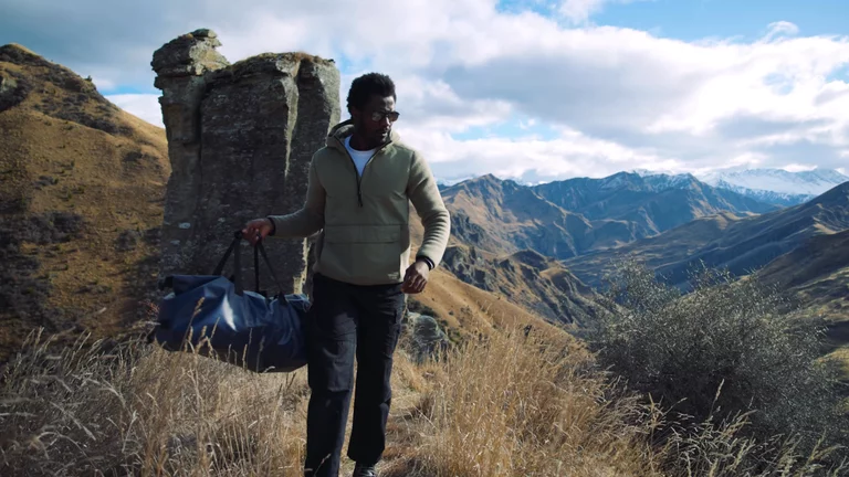 Video of man walking on mountain hike carrying duffle bag on his shoulder