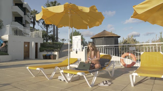 A girl working on her laptop while sitting on a deckchair at a resort