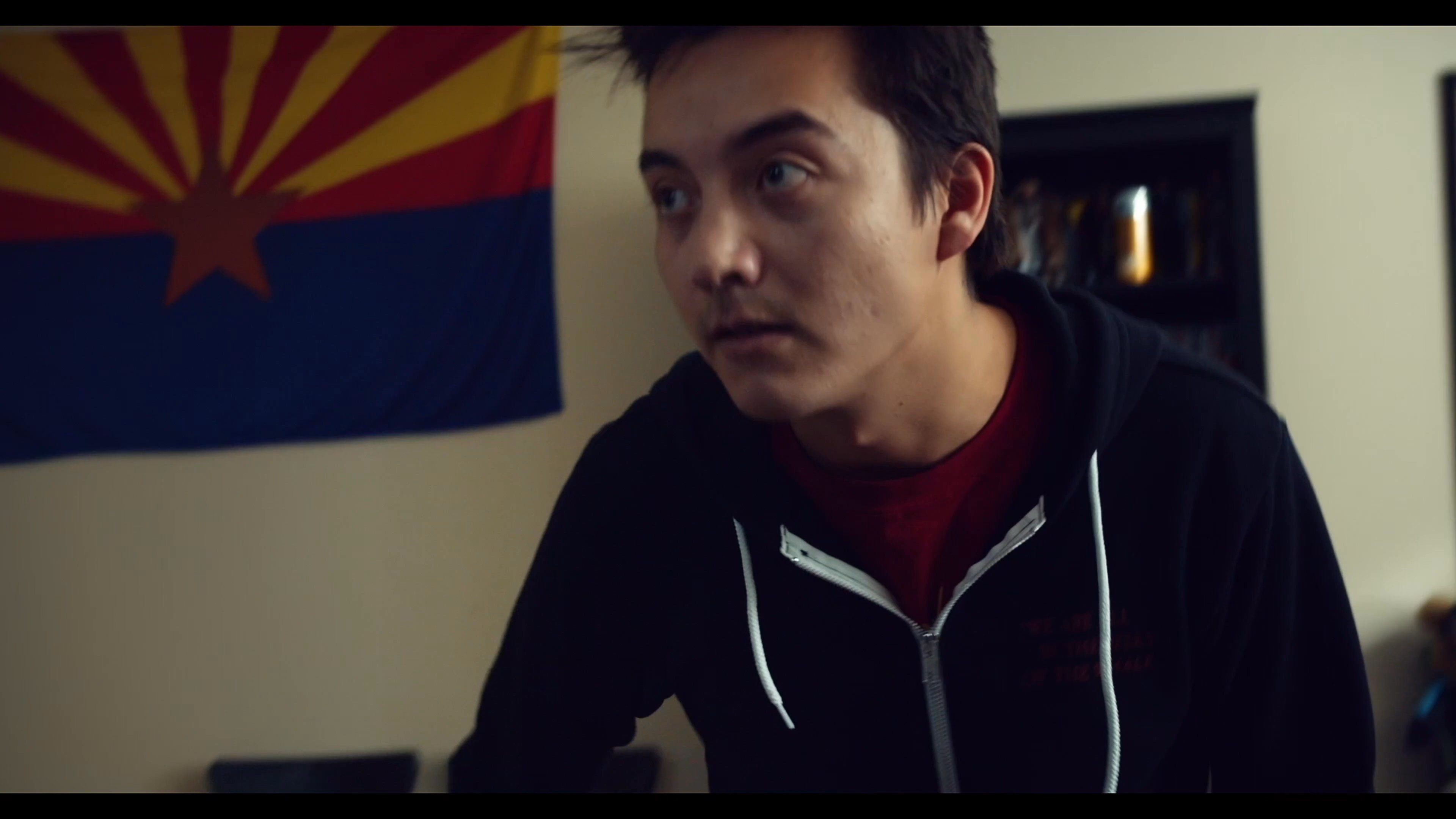 Two young men engage in a lively conversation in a residential space, featuring a lighthearted moment involving a baseball bat.