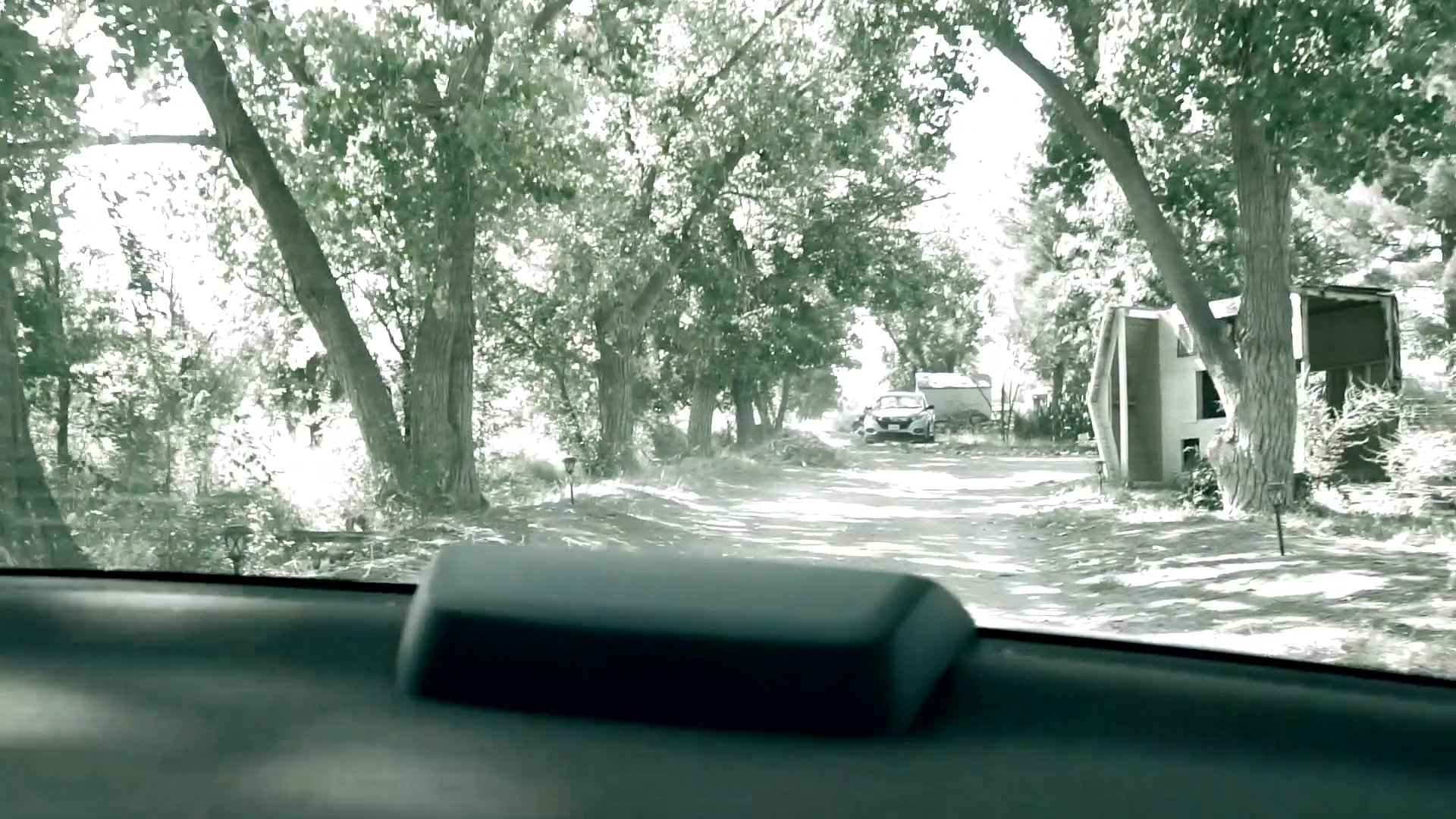 A vehicle drives away from a rural property, transitioning from a view of the house into a tree-lined driveway.