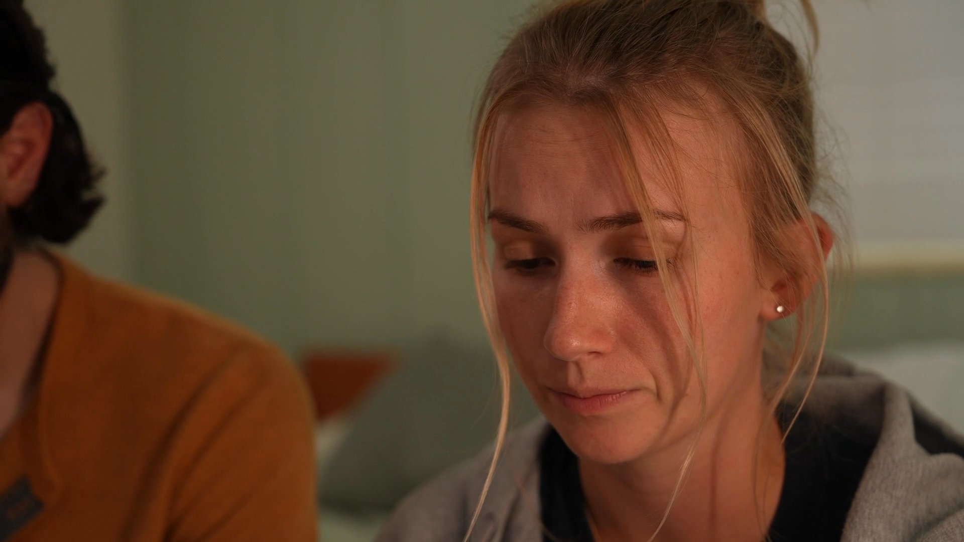 A man and woman sit together in a bedroom, sharing a focused and emotionally charged conversation. They maintain eye contact and demonstrate attentive body language as they navigate a significant interpersonal exchange.