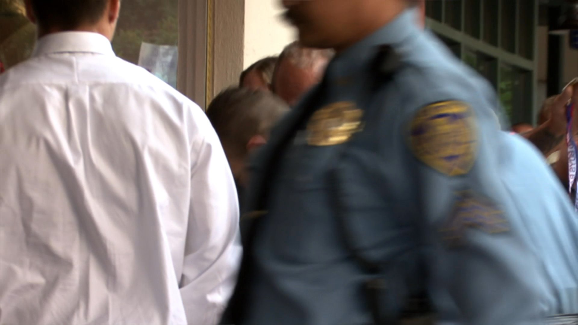 Law enforcement officers manage a security checkpoint, screening individuals for entry into an organized event by checking wristbands.
