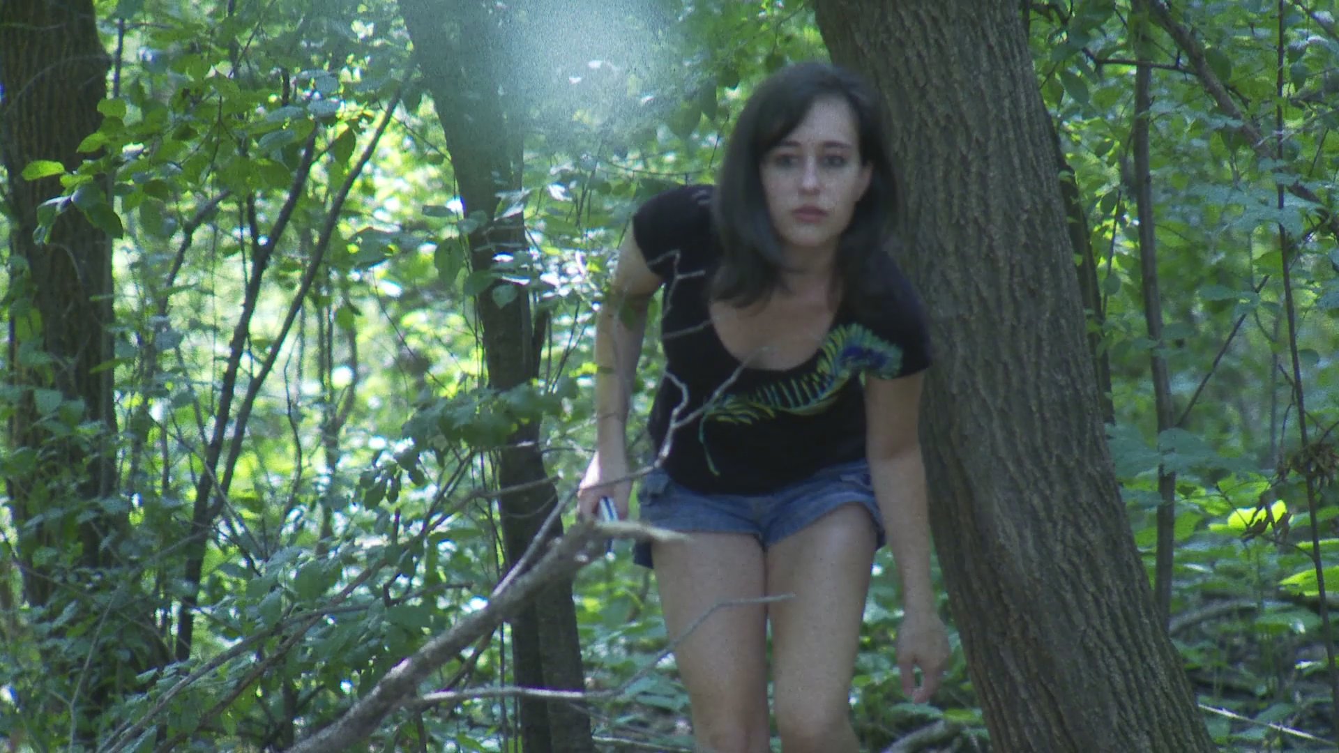 A woman appears distressed while using a mobile phone in a wooded area before abruptly moving into a residential dining room setting. Her transition suggests a shift from an isolated, possibly urgent situation to an indoor environment.