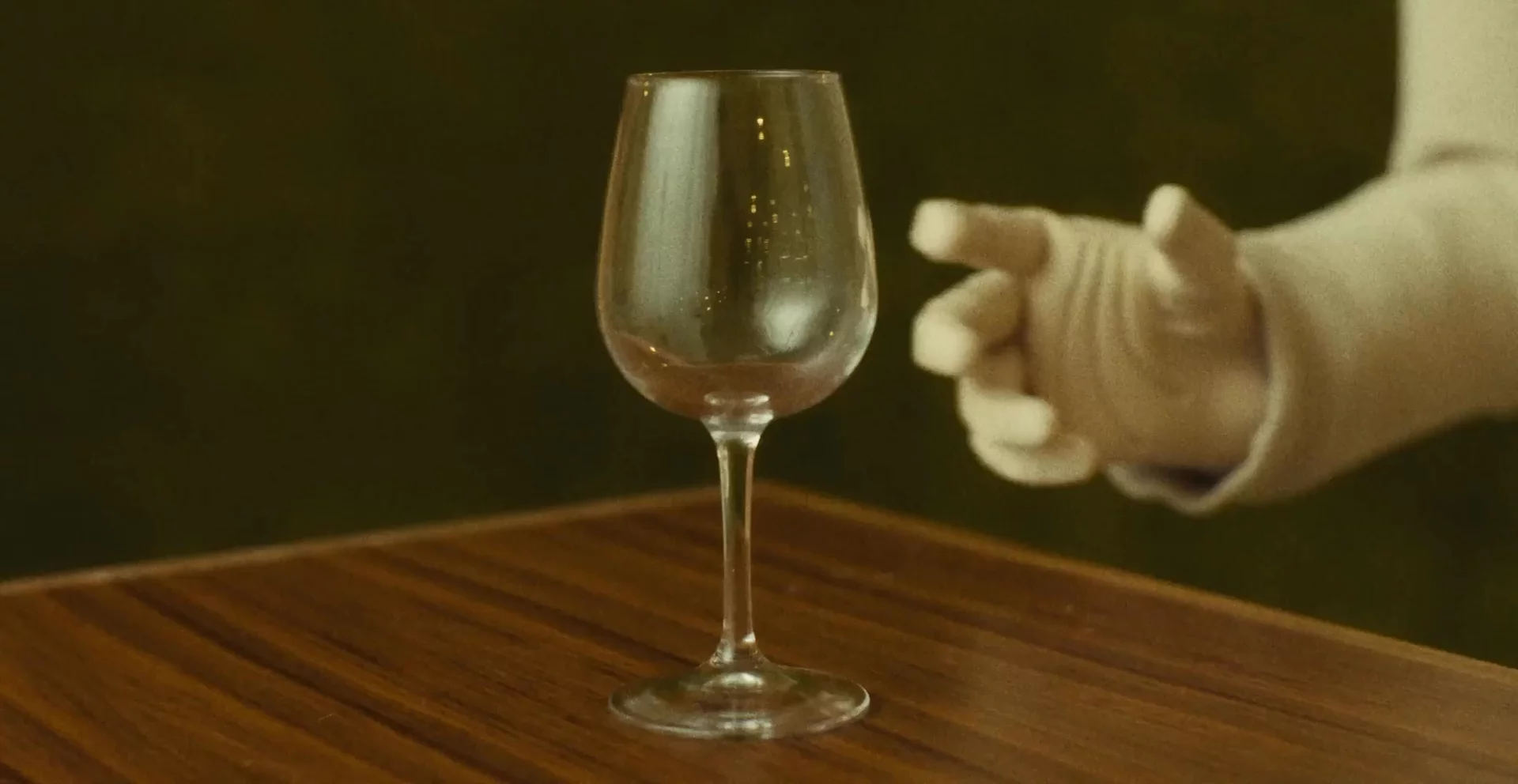 A NEO robot hand reaching toward the stem of a wine glass.