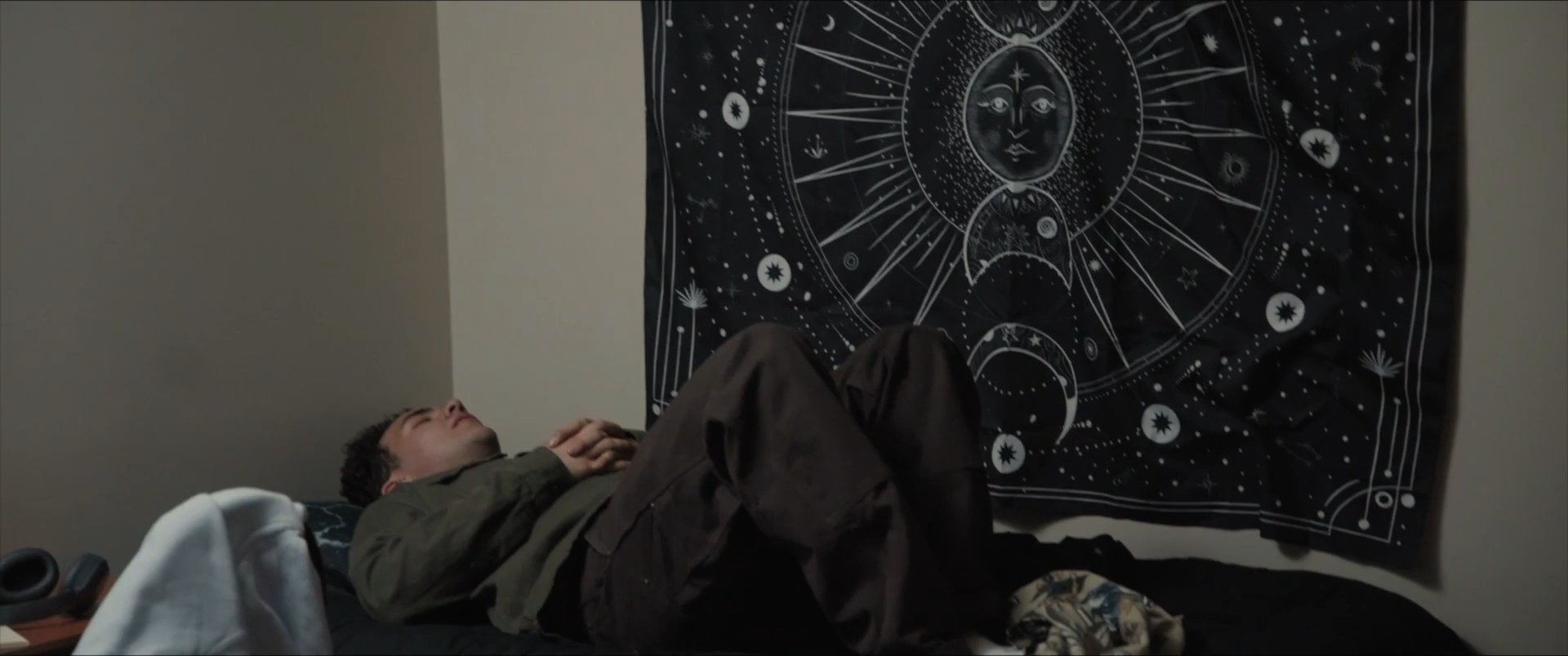 A man navigates different moments of downtime within his living space, transitioning from standing to resting on a couch and eventually lying in bed.