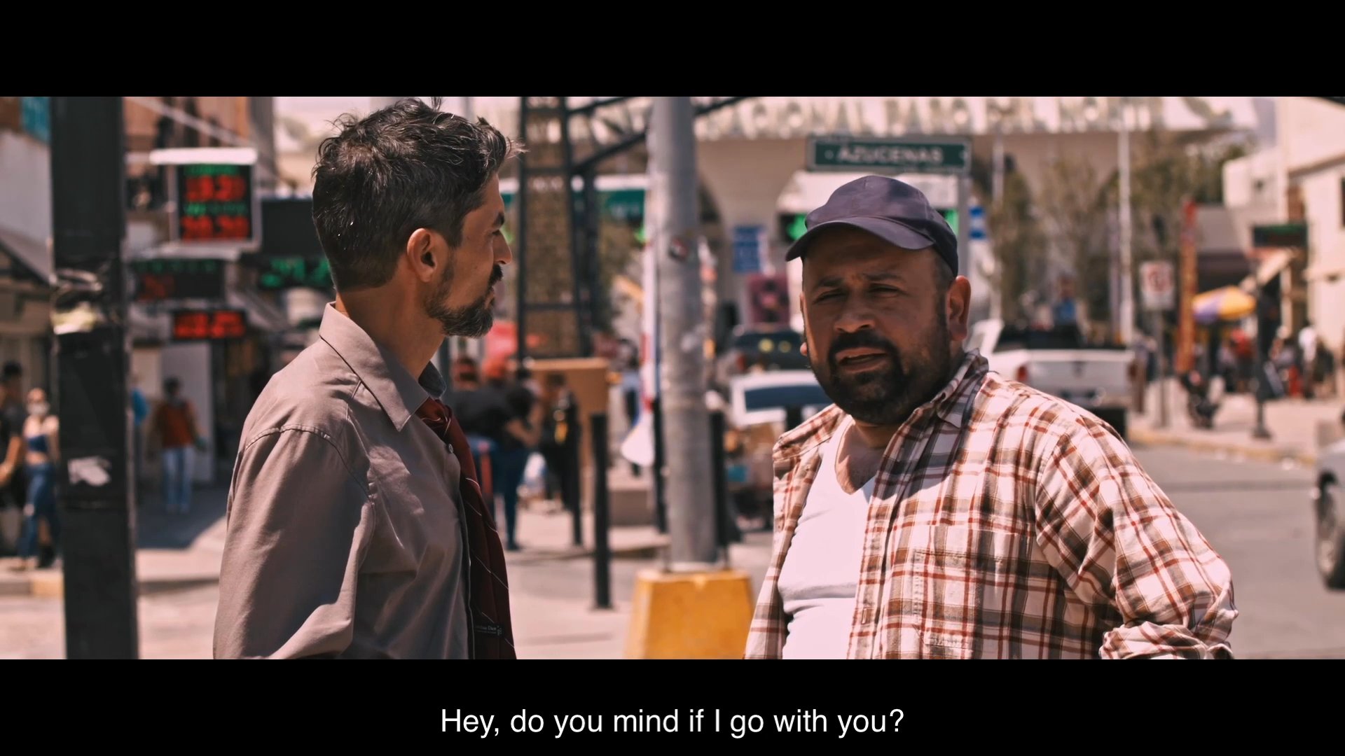 Two men discuss crossing the border at a busy urban street junction while engaging in a hesitant, personal dialogue about their intentions.