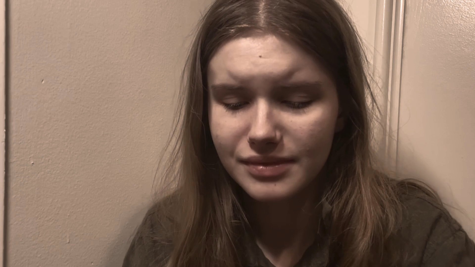 A woman exhibits raw emotional distress and vulnerability while speaking in a solitary indoor setting. She displays various facial expressions of sorrow and contemplation throughout the sequence.