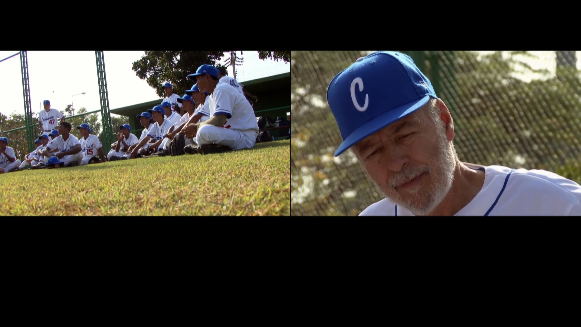 A coach provides instructional guidance to baseball players gathered on a field during a training session. The team members observe closely as the coach demonstrates proper techniques and positioning.