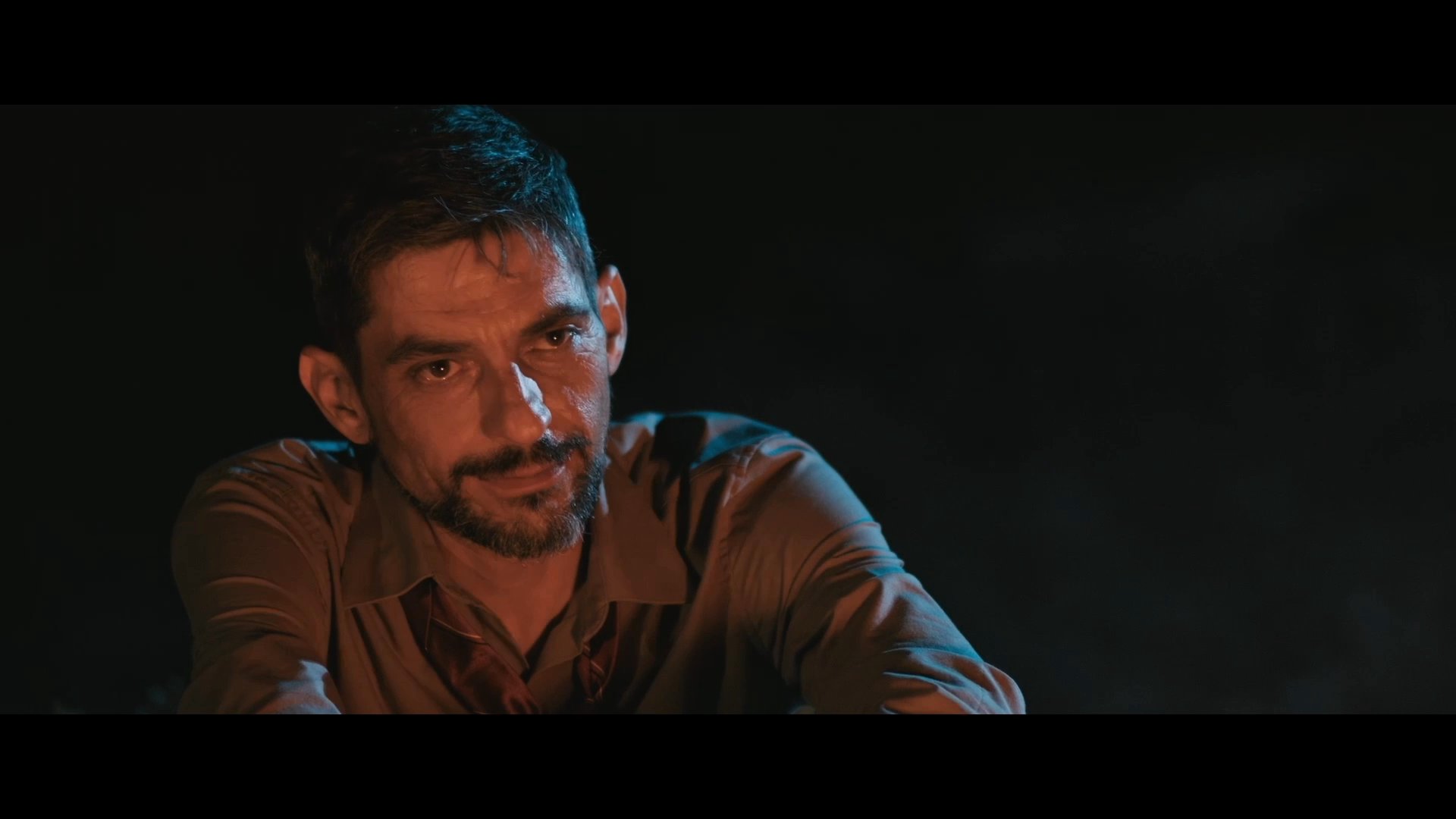 Two men exchange a lighthearted conversation by a campfire at night, concluding with a pun about nails and bread.