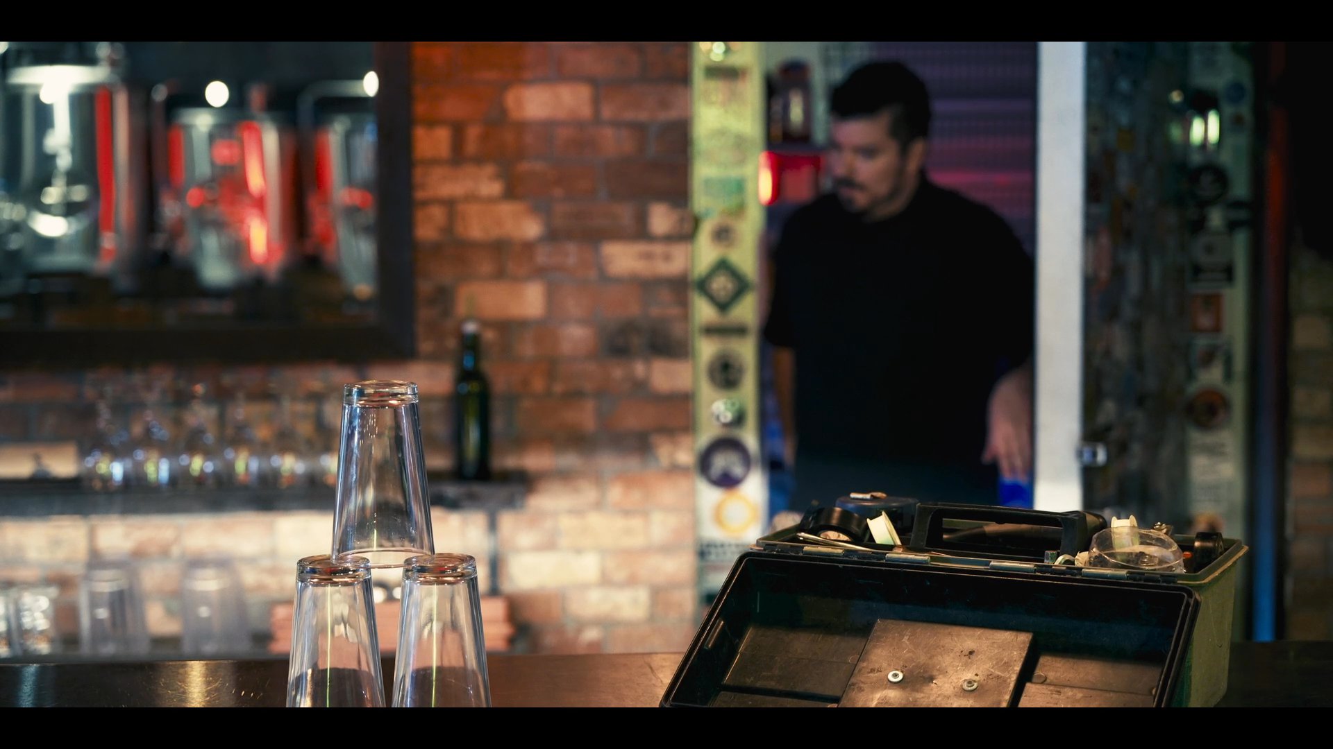 A bartender transitions from a storage room to a bar area to retrieve and handle maintenance equipment for service preparation.