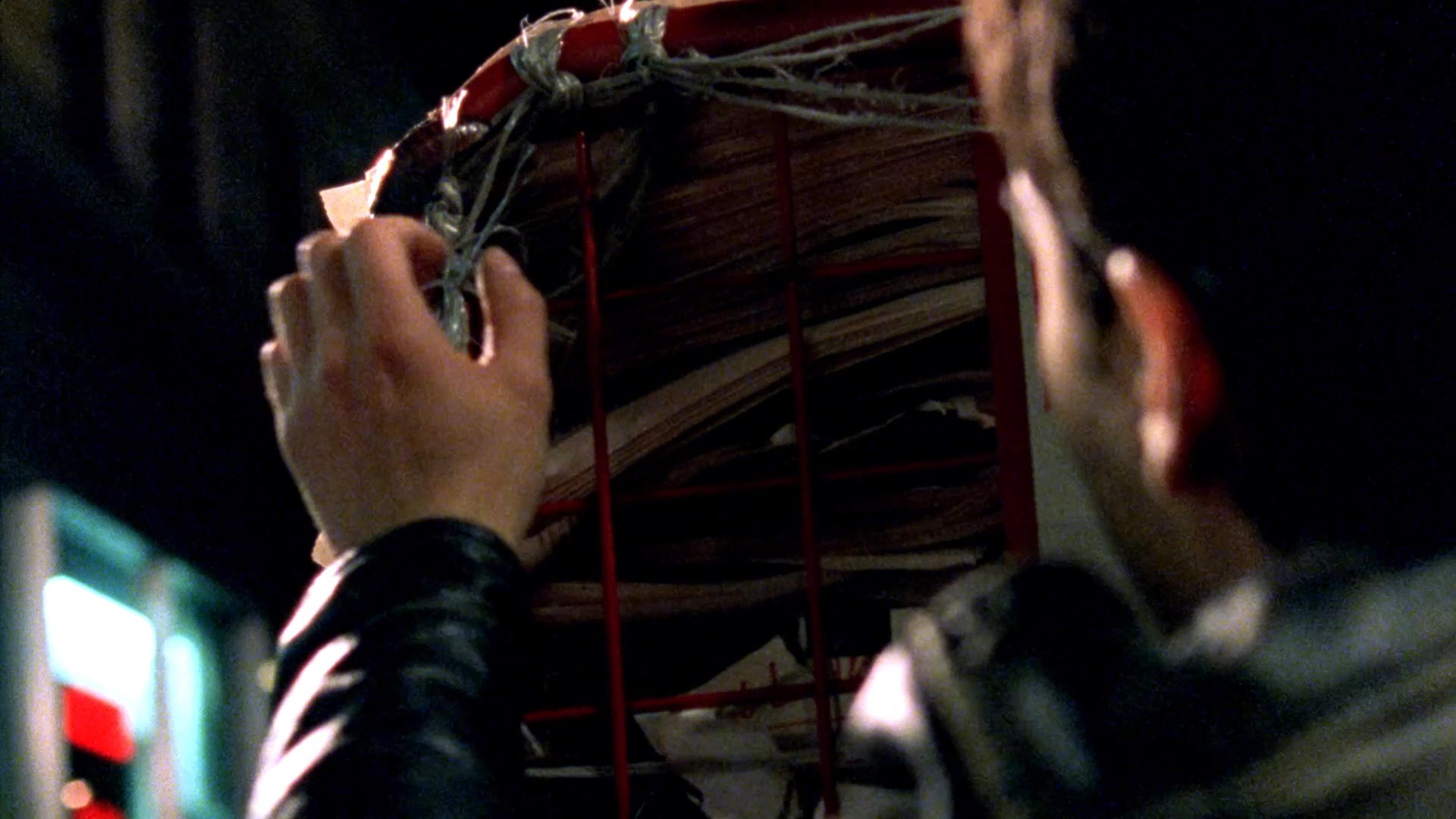 A man reacts with alarm after discovering a large cockroach resting on a stack of newspapers inside an urban setting at night. He retreats slightly, visibly shaken by the encounter.