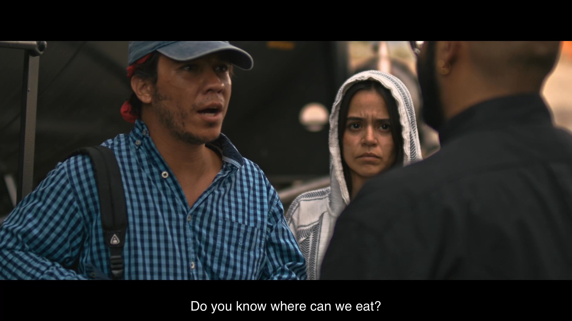 A cleric offers food, shelter, and rest to two travelers near a train line, assuring them of their safety despite their concerns about missing their transport.