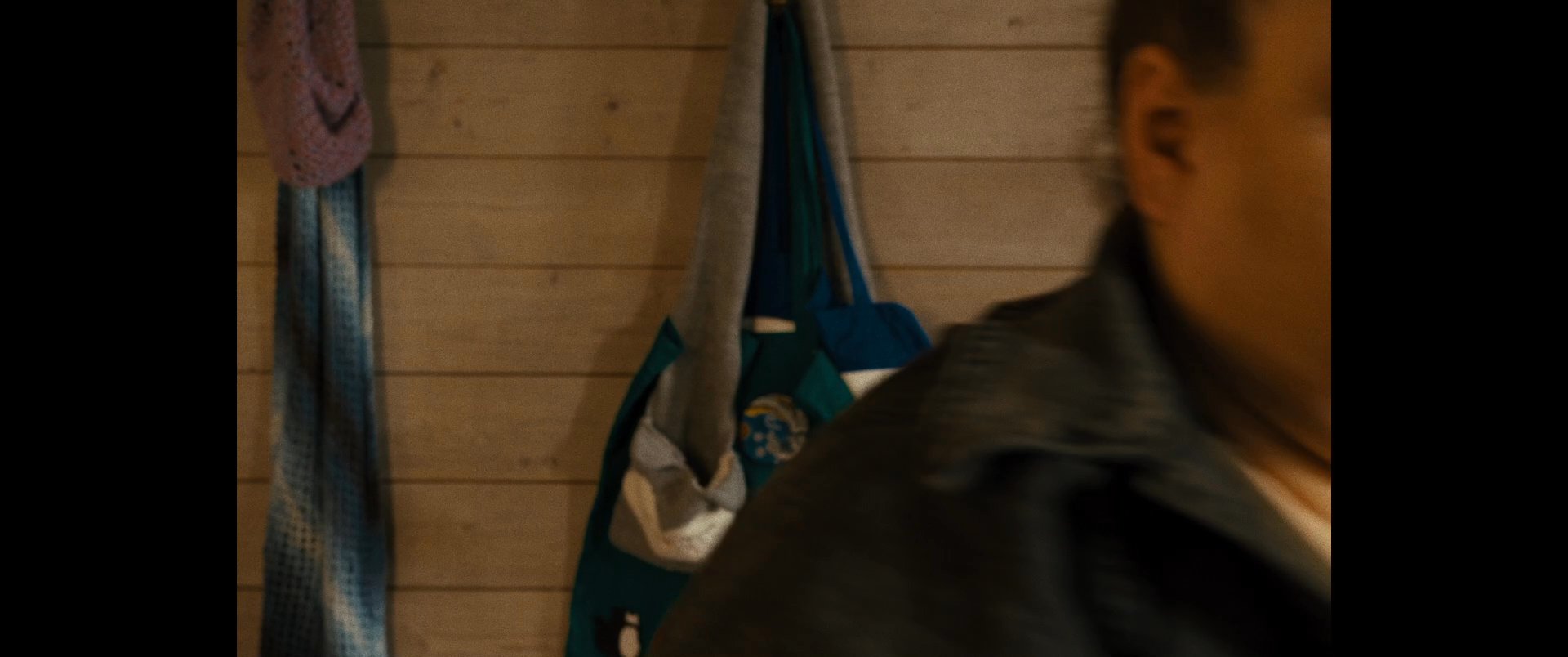 An individual prepares for departure in a domestic kitchen by gathering personal items including a thermos and a patterned tote bag. The scene captures the transition from indoor activity to movement.