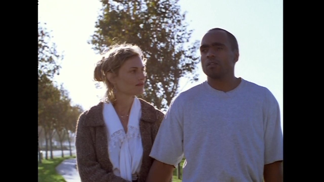 A man and woman walk together through a park setting while engaged in an ongoing conversation.