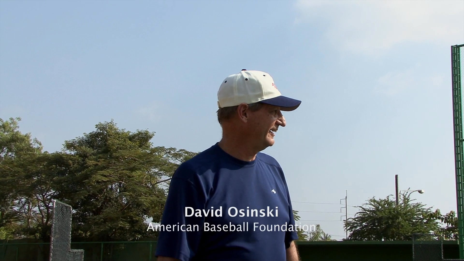 Professional coaches instruct a group of young baseball players on fundamental techniques and mechanics at an outdoor field training session.