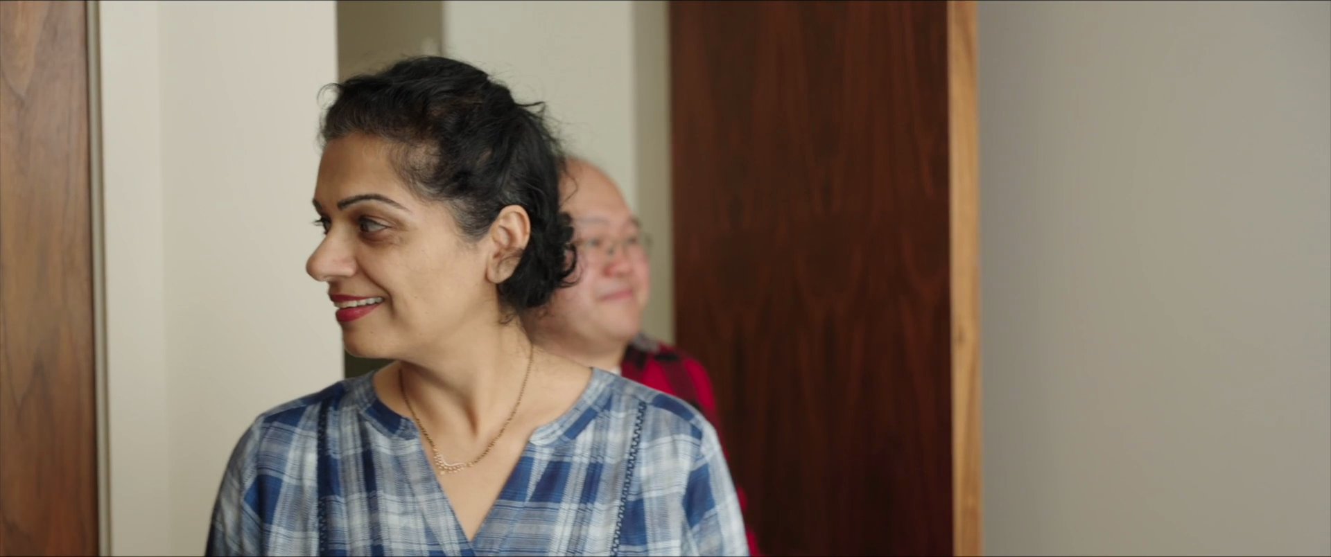 Aerial shots of a San Francisco urban neighborhood transition to a group of guests arriving at a hotel room door and interacting with someone inside.