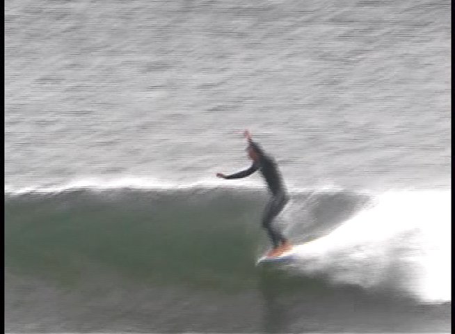 A surfer in a wetsuit maneuvers a surfboard across the face of an incoming ocean wave.