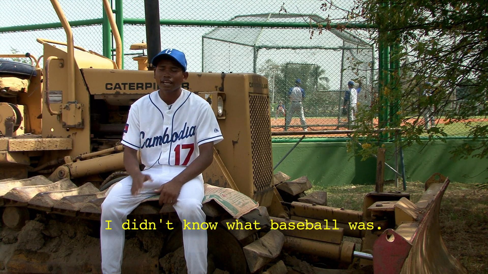A coach demonstrates baseball techniques to a team on a field, interspersed with a player sharing his personal history with the sport during an interview.