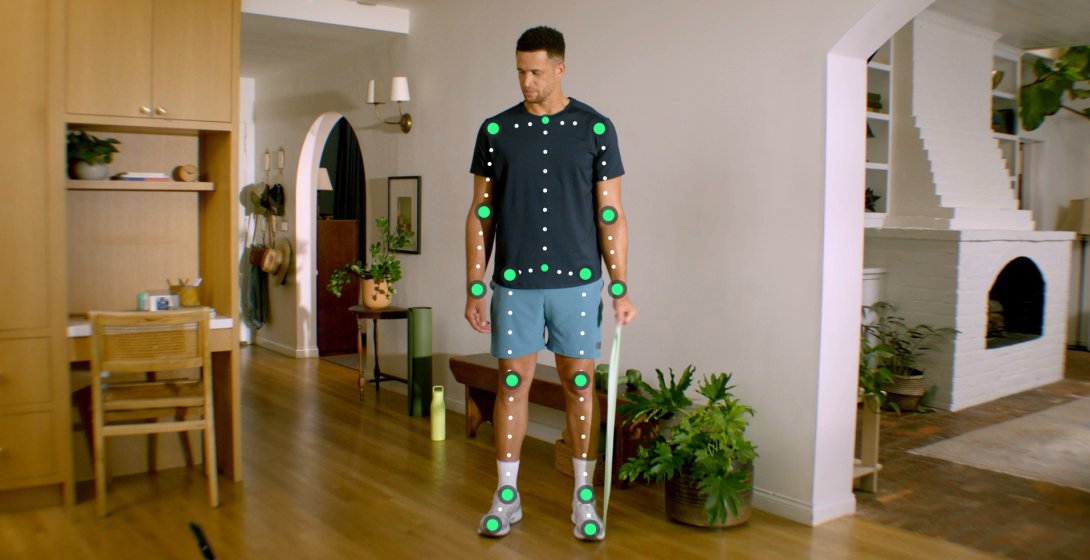 A young man stands in his living room practicing some strengthening and flexibility exercises with a resistance band. 