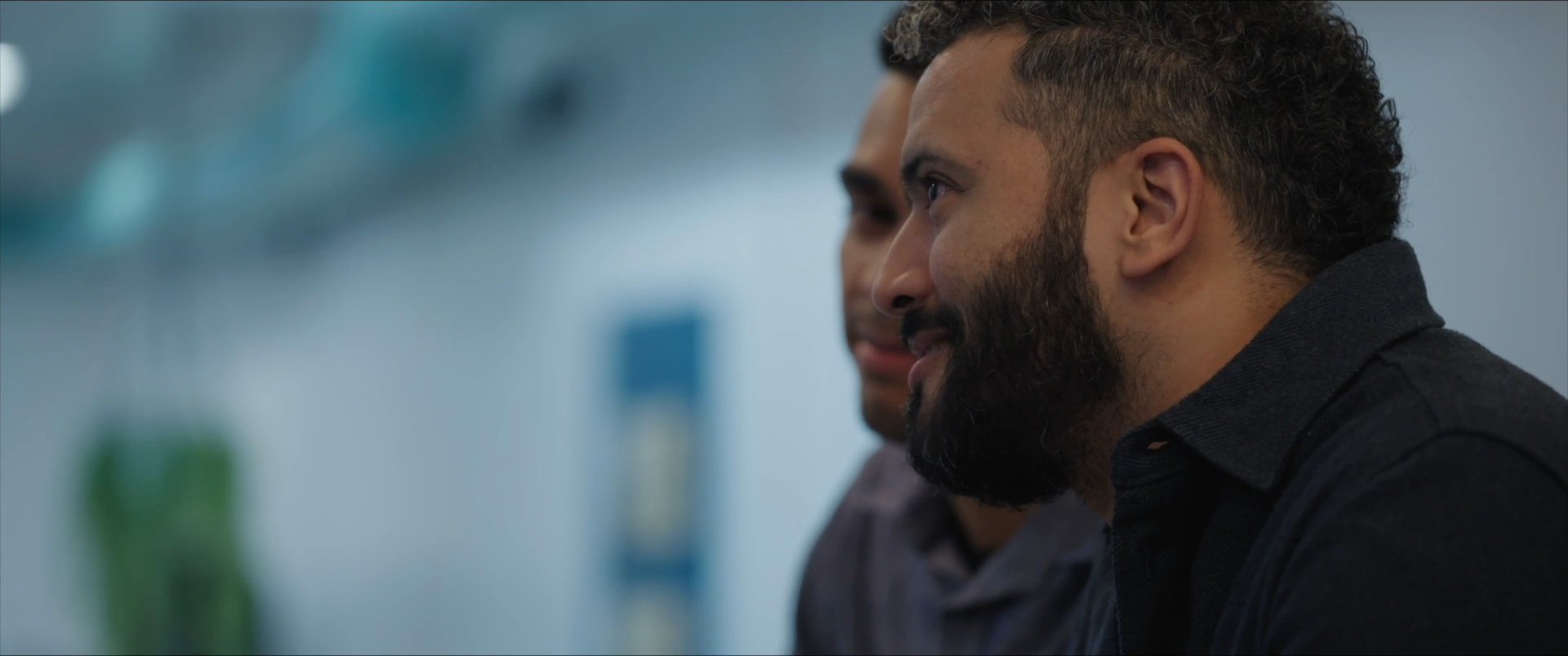 Two men engage in a focused, professional conversation within an office environment. The exchange alternates between speakers as they address one another during a structured meeting.
