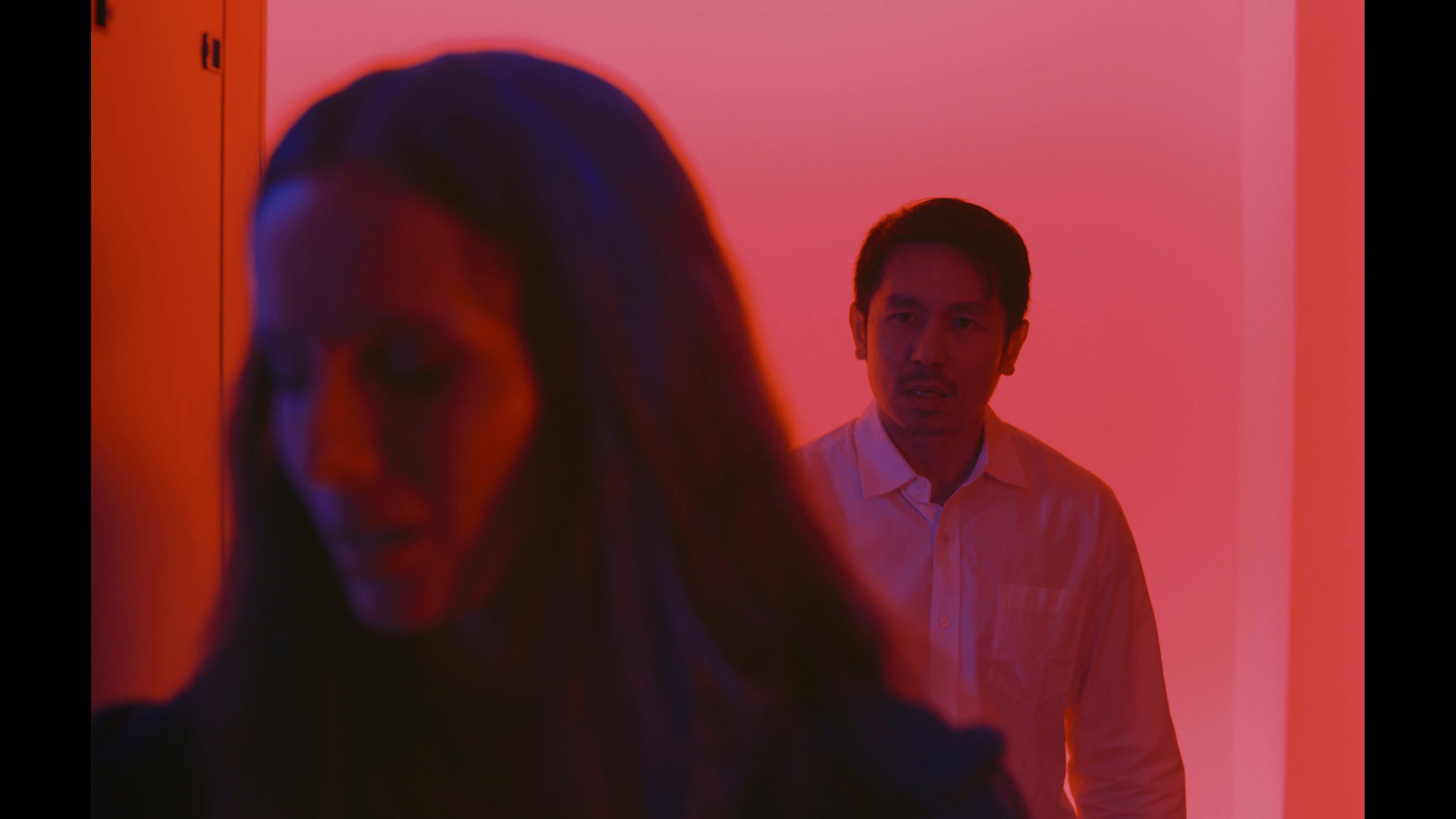 Two professionals conduct a technical assessment within a server room bathed in red atmospheric light. The individuals engage in a focused discussion while inspecting the hardware infrastructure.