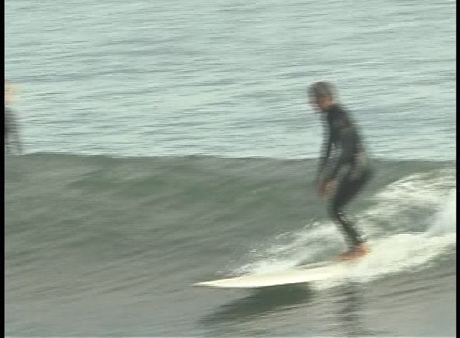 A surfer in a black wetsuit skillfully navigates multiple ocean waves while standing on a surfboard. The sequence captures the fluidity and balance maintained during the ride.