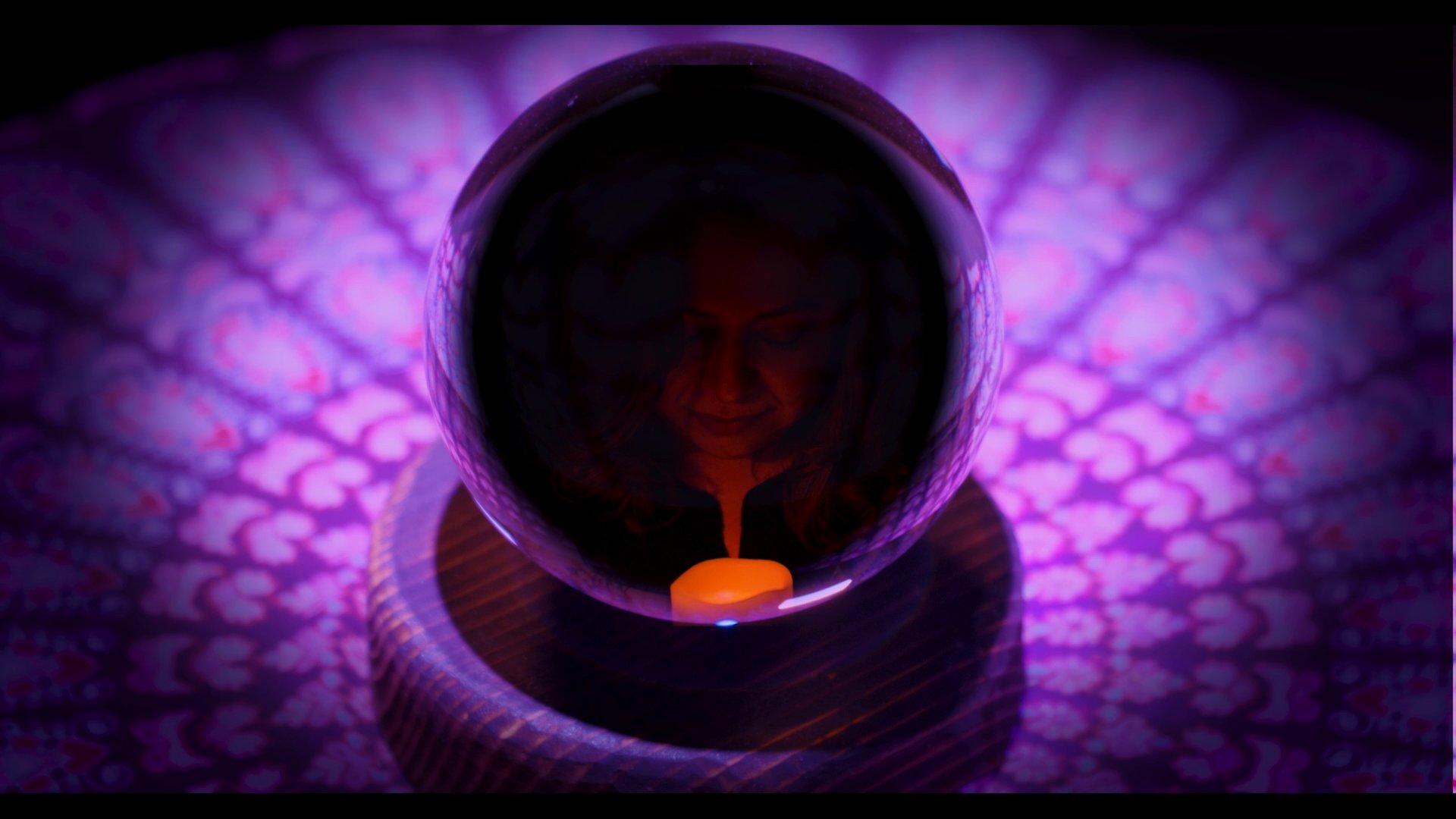 A medium conducts a reading using a crystal ball, capturing the spiritual practitioner's reflection as she stares into the glass orb. The scene emphasizes an atmosphere of mystery and divination through close-up shots of the illuminated crystal.