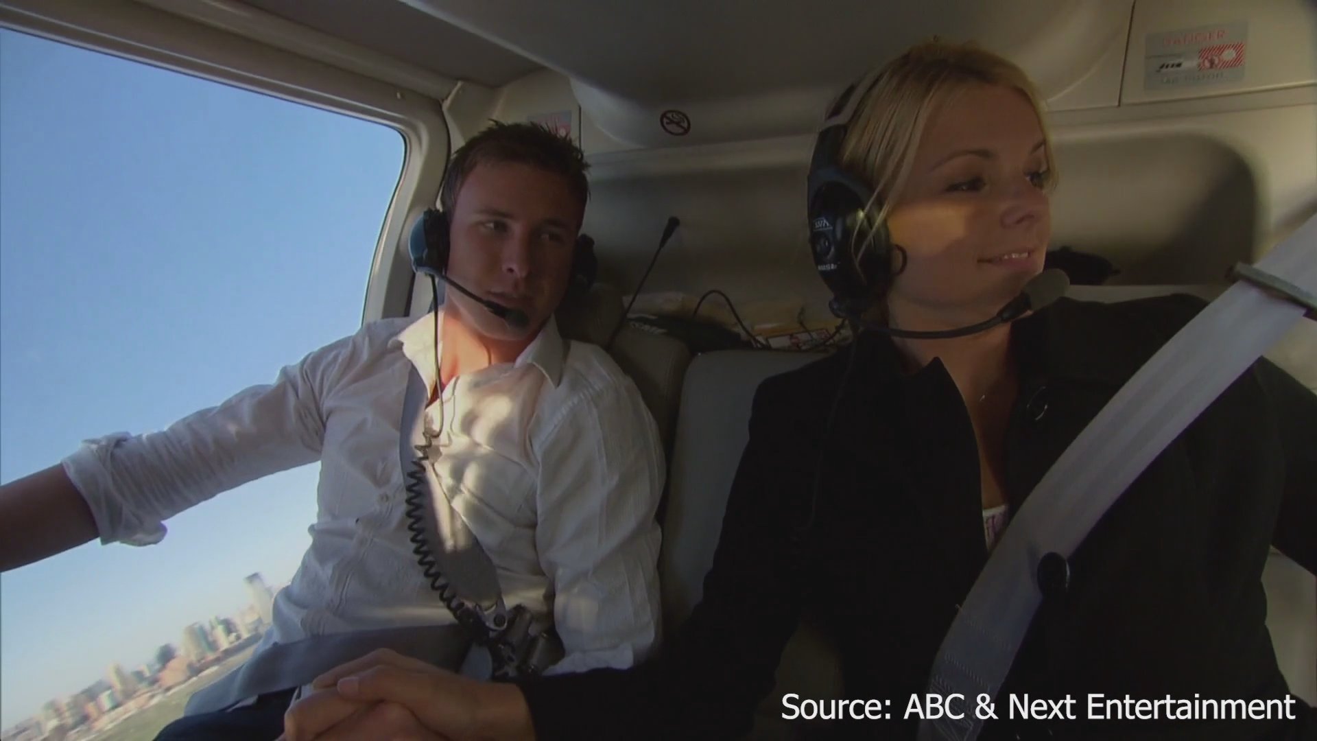A couple tours New York City by helicopter, taking in aerial views of the Manhattan skyline and the Statue of Liberty.