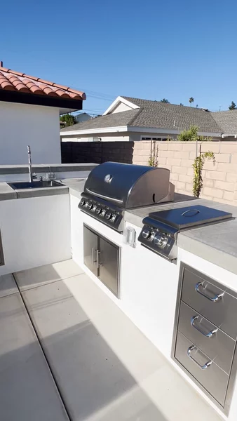 Custom outdoor kitchen build featuring built-in grill, concrete countertops, sink, and mini fridge