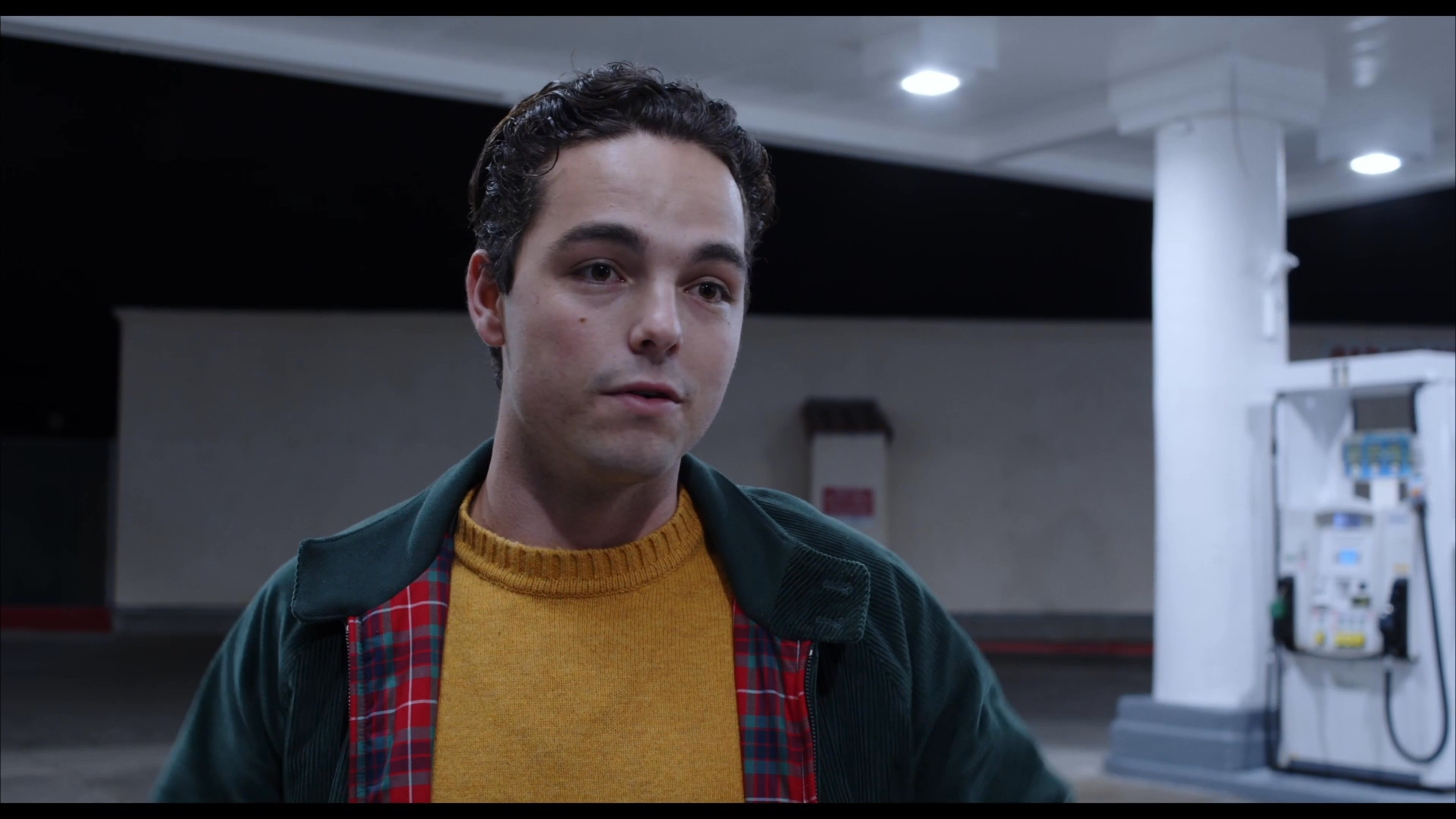 Two young men engage in an animated discussion while positioned near a vehicle at a gas station during the night.