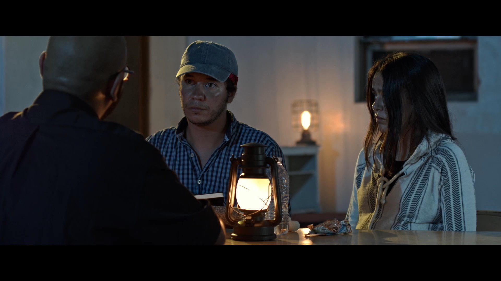 A priest gives urgent advice to a young man in a dimly lit room, instructing him to maintain secrecy and exercise caution. The scene underscores a somber exchange regarding the young man's decision to leave and seek support from the church.