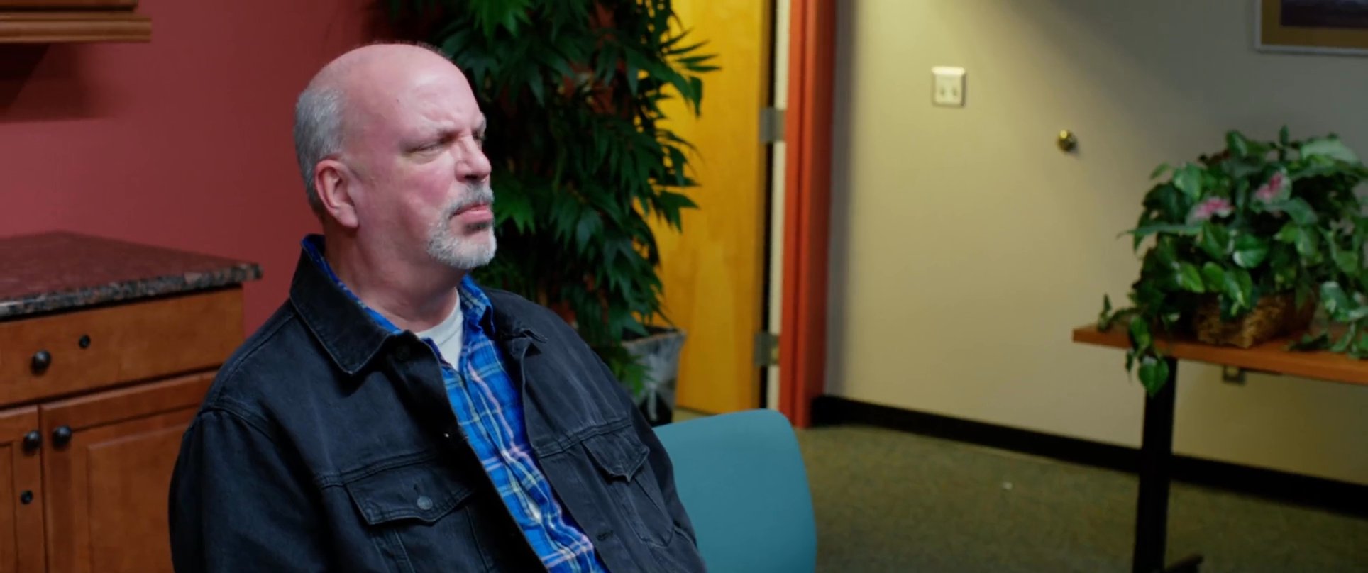 An intense verbal dispute between two men escalates into a physical altercation within an office waiting area as others observe.