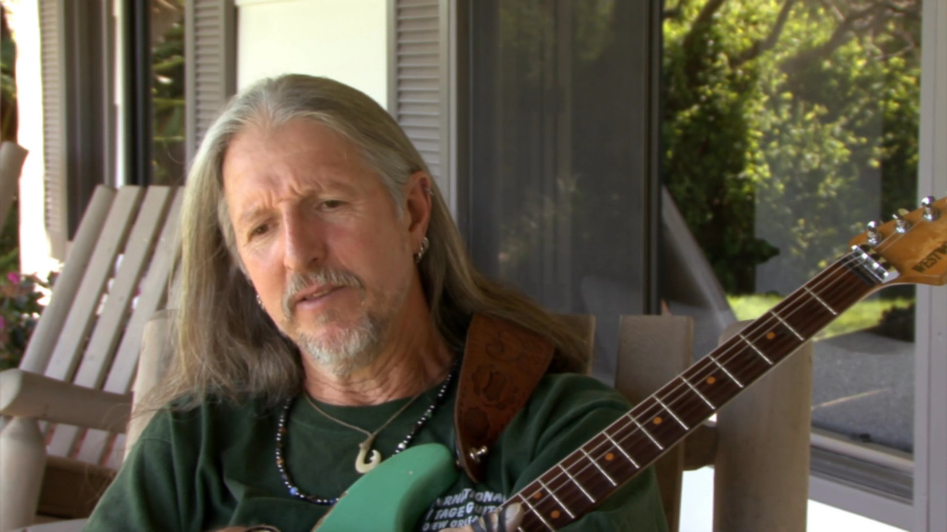 Musician Pat Simmons of The Doobie Brothers shares insights during an interview while playing an acoustic guitar on a sunlit porch.