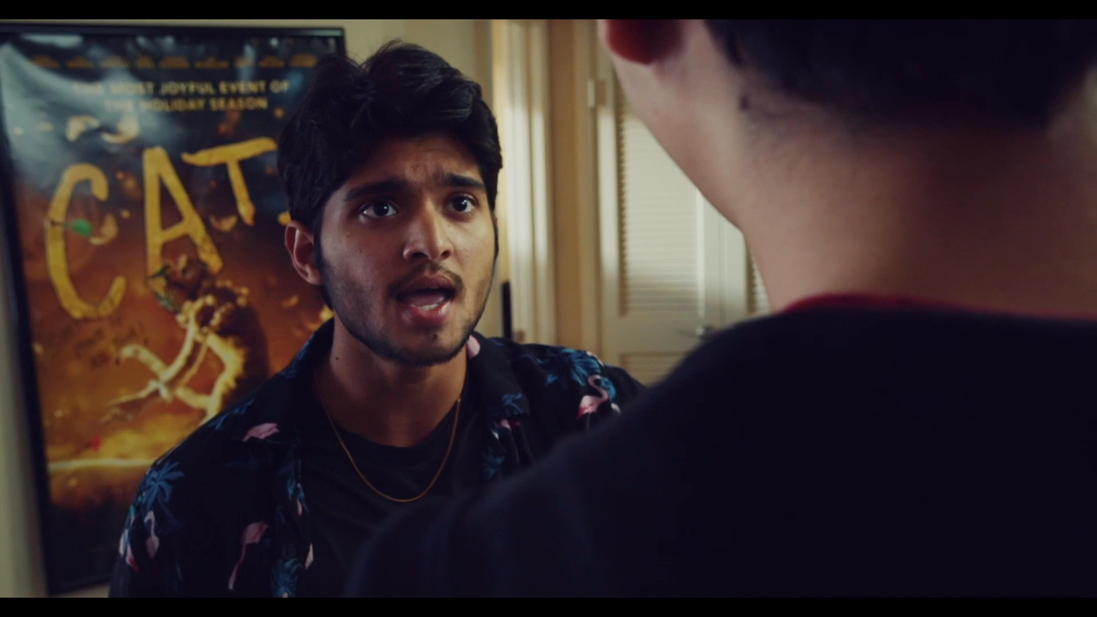 Two young men engage in a tense and heated confrontation within a domestic living space, while a third individual observes from the background. The interaction escalates through expressive body language and confrontational dialogue.