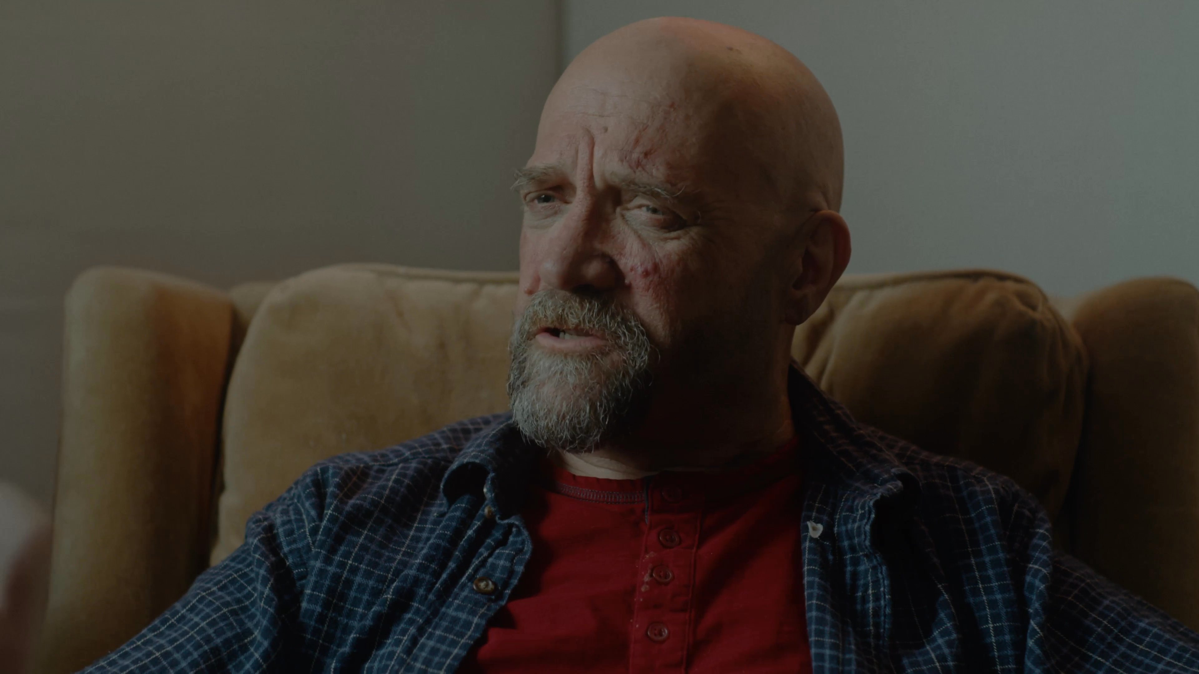 Two men engage in an earnest conversation while sitting in a living room, alternating between listening and speaking with expressive gestures.