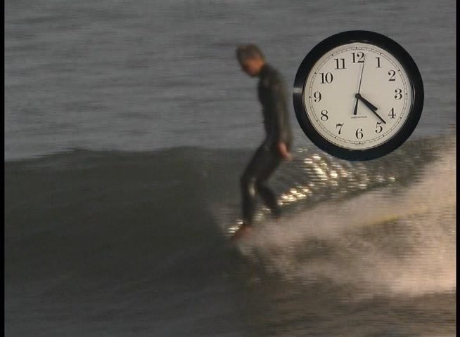 Surfers ride waves in the ocean while wearing wetsuits, demonstrating athletic skill and balance. The footage emphasizes the motion of the water and the technique of the surfers.