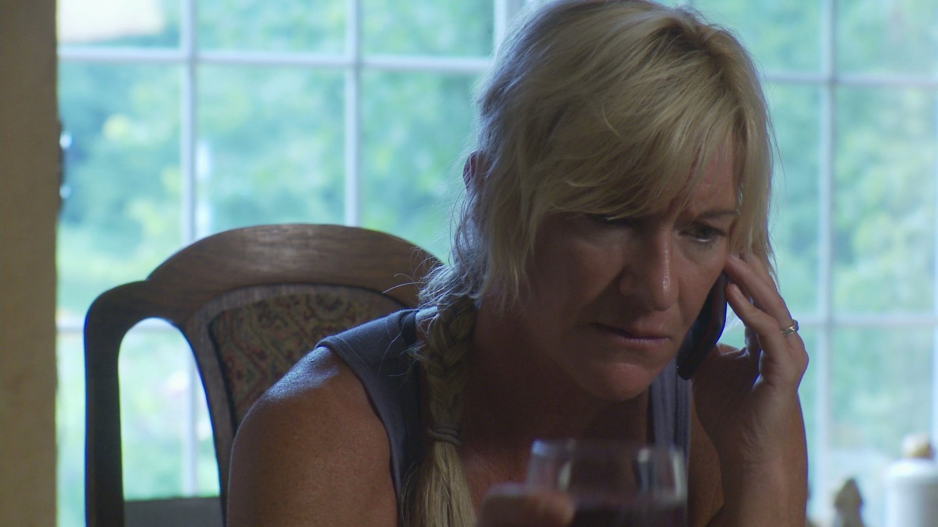 A woman displays visible signs of emotional distress while engaged in a tense telephone conversation at home. She holds a glass of wine and appears increasingly concerned or upset as the call progresses.