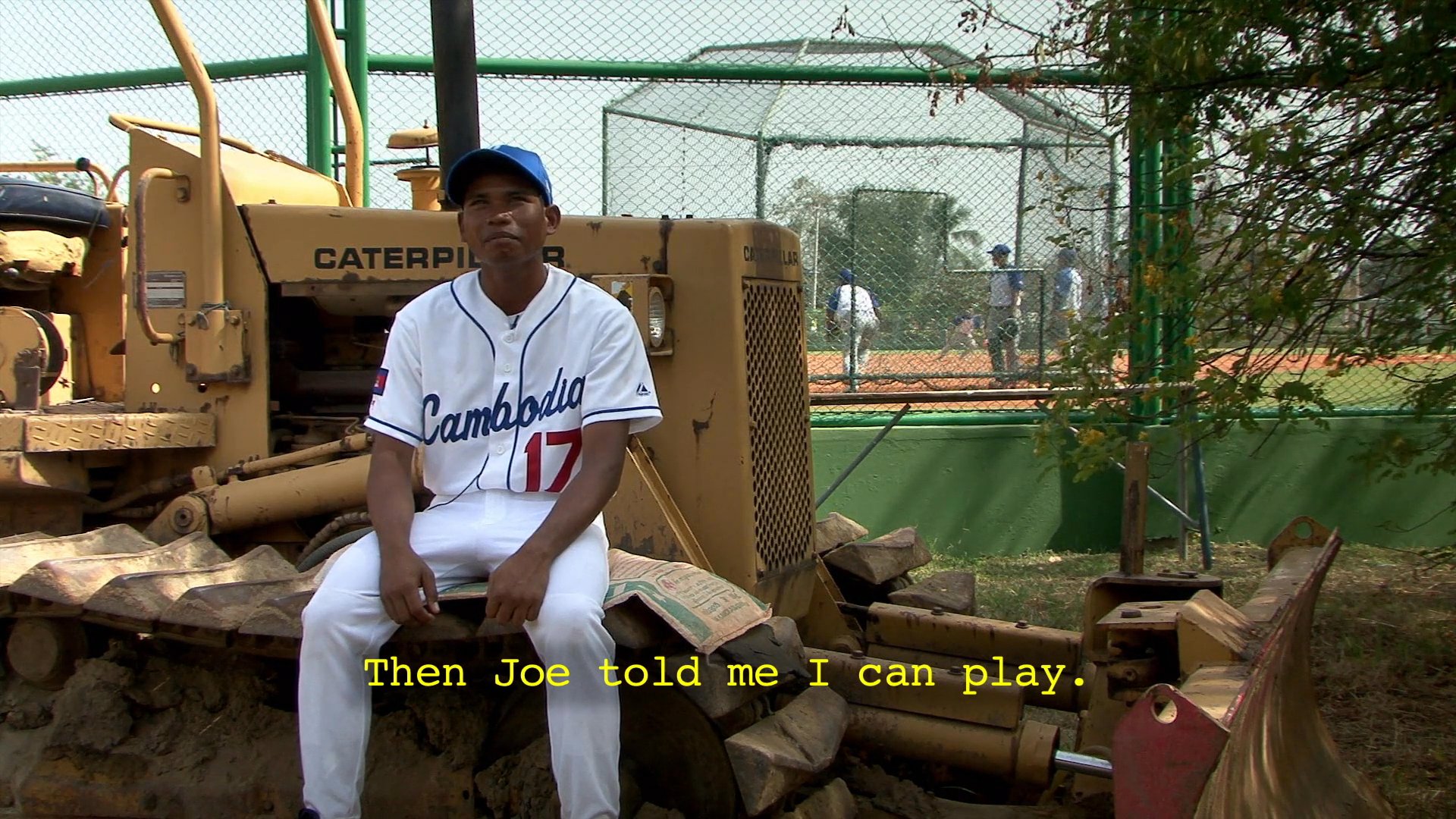 A young athlete recounts his introduction to baseball while sitting on construction equipment, followed by scenes of a coach instructing a team on a field.