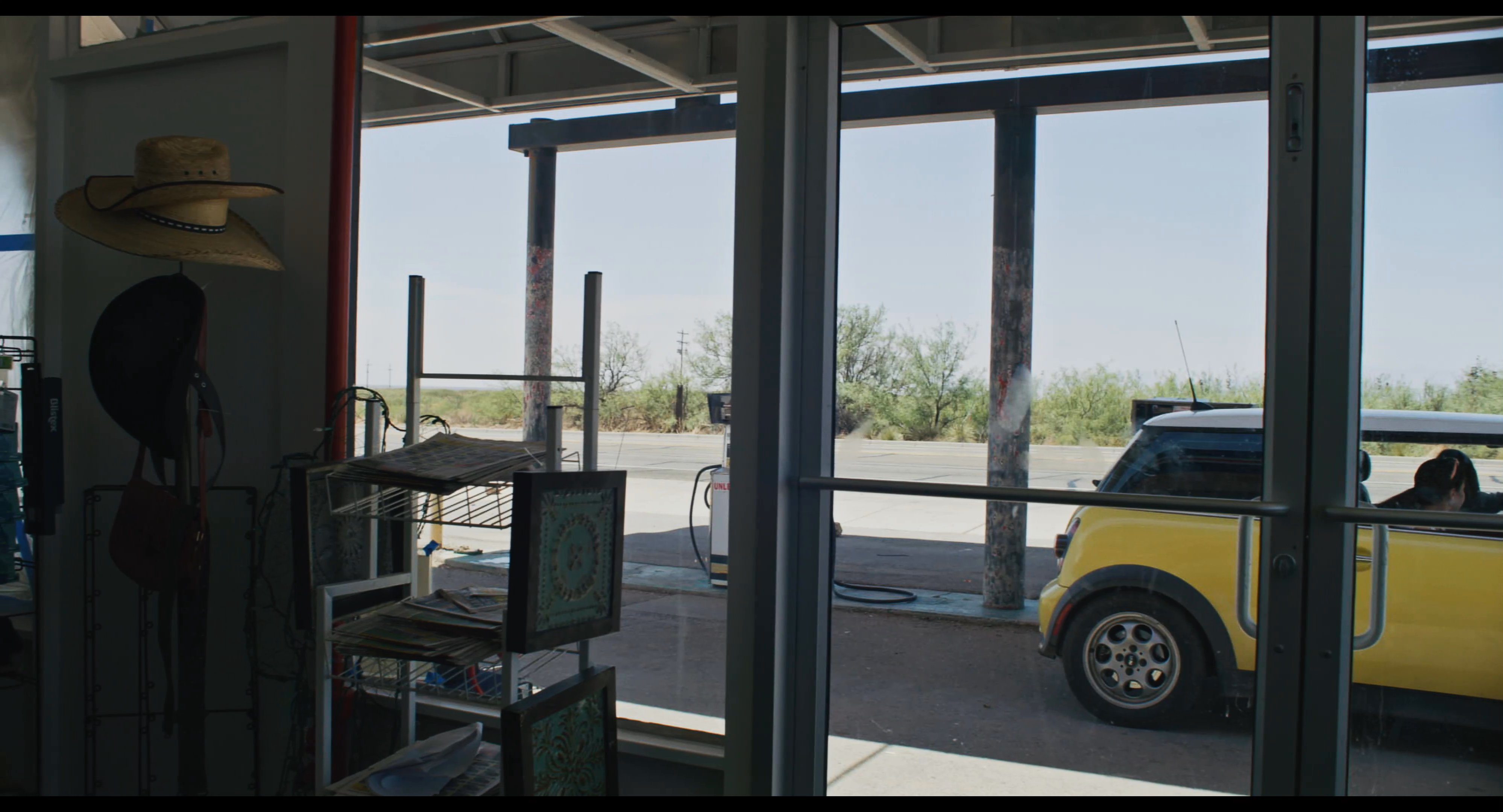 A traveler in a yellow vehicle stops at a desert gas station to refuel and reorganize before continuing her journey.