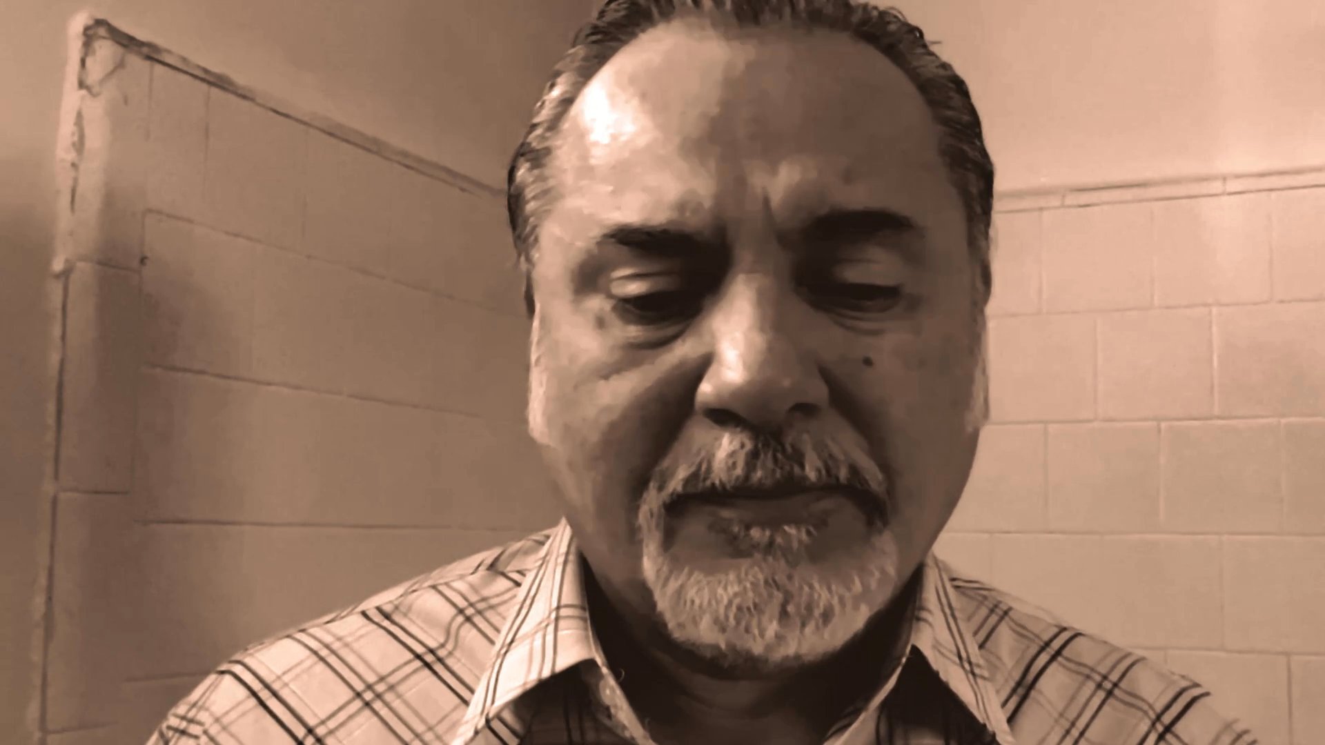 A middle-aged man with a goatee speaks directly into the camera with a serious and contemplative demeanor.