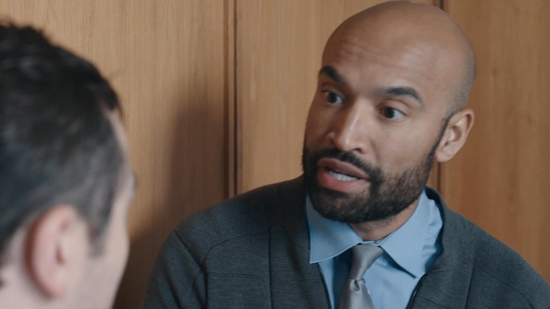 Two male colleagues engage in an intense, close-quarters conversation in an office setting, transitioning from a discussion to a more confrontational interaction.