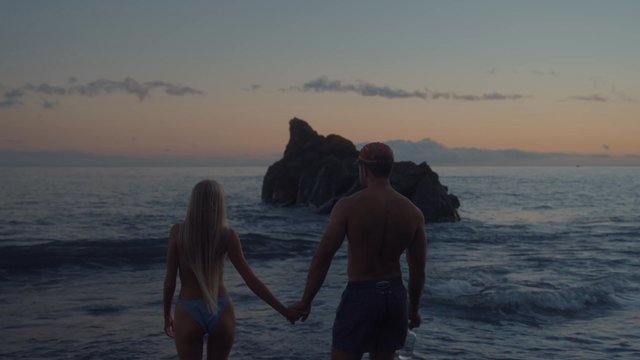 A couple walking and embracing by the shore.