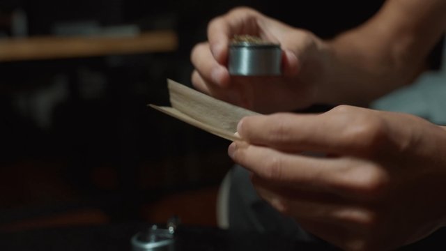 A man scattering weed from a grinder into rolling paper