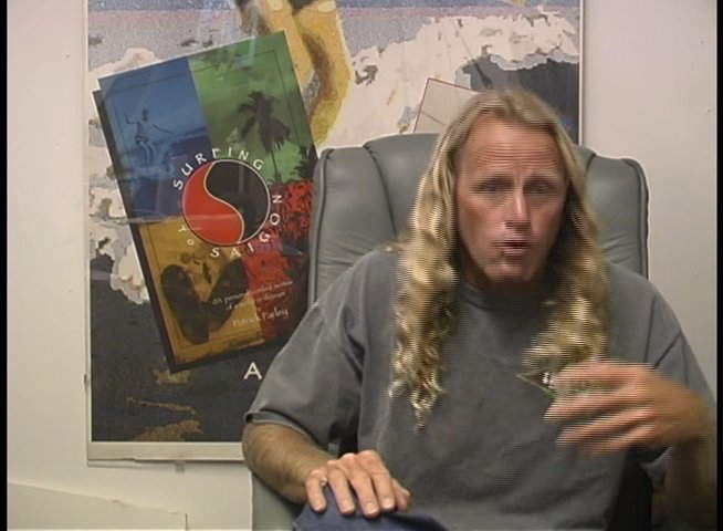A long-haired man sits in an office setting and engages in an animated discussion, using expressive hand gestures to emphasize his points. He presents a narrative while speaking directly to an off-camera interviewer.