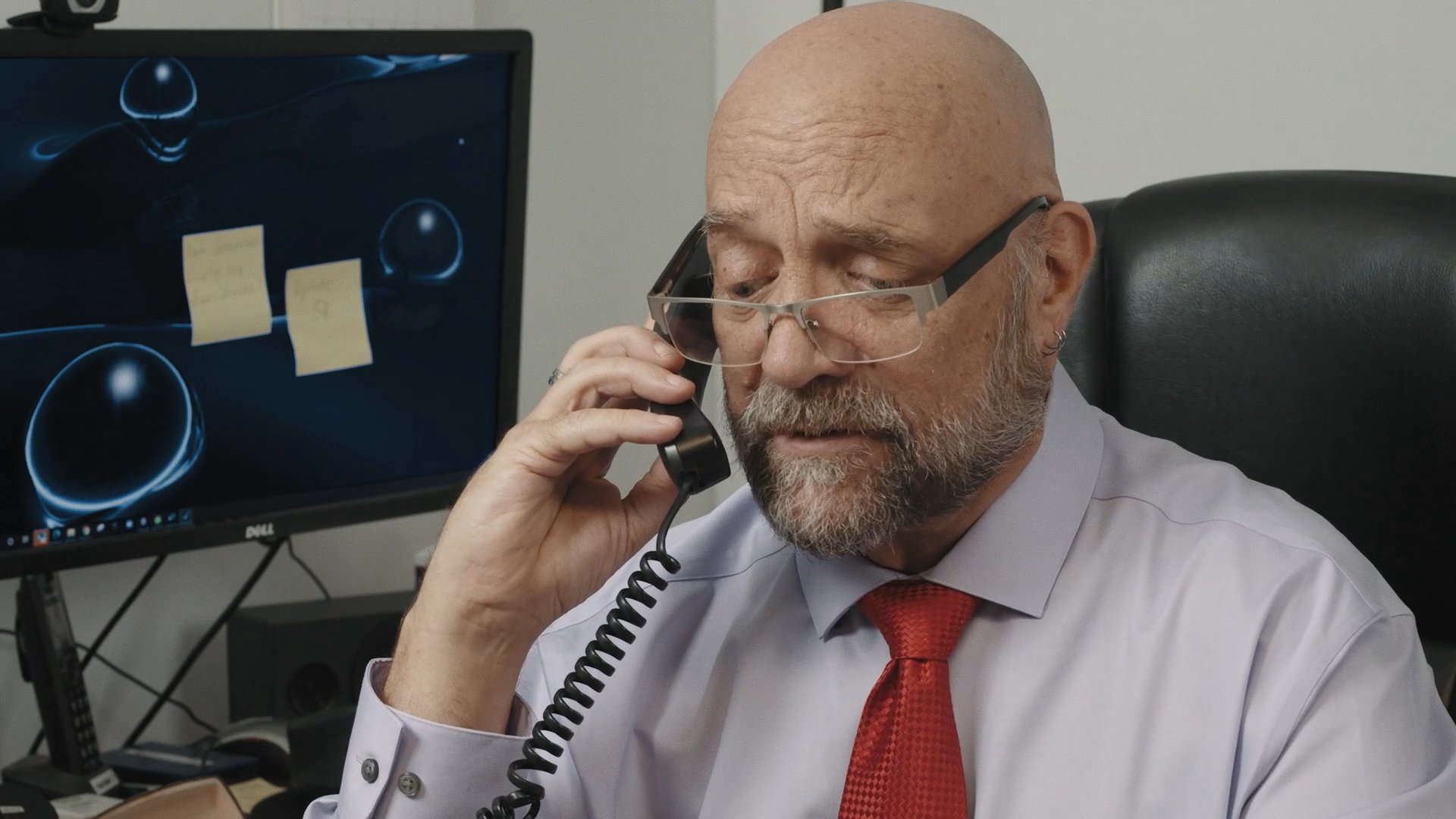 A professional man in an office and a woman in a separate room engage in a simultaneous telephone conversation. Both individuals appear focused and intent as they communicate over their respective devices.
