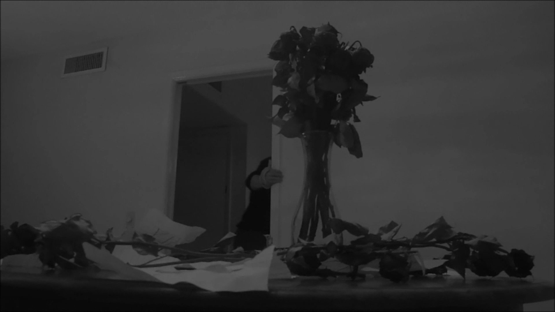 A man experiences deep emotional distress and grief within a kitchen setting, surrounded by scattered roses. He reflects on a photograph before collapsing in physical and mental exhaustion.
