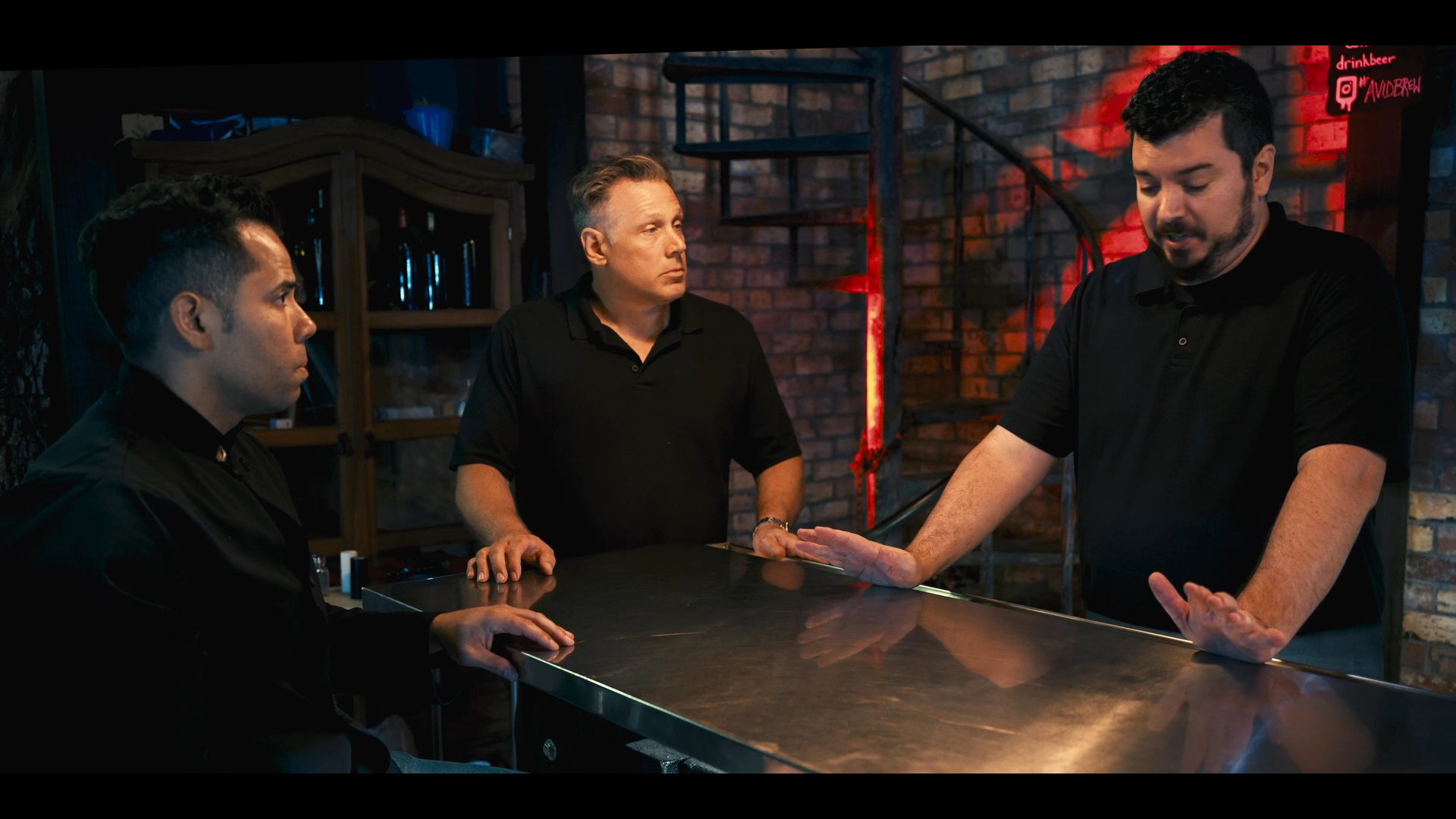 Three individuals engage in a focused, collaborative discussion at a metallic table in a professional, dimly lit setting.
