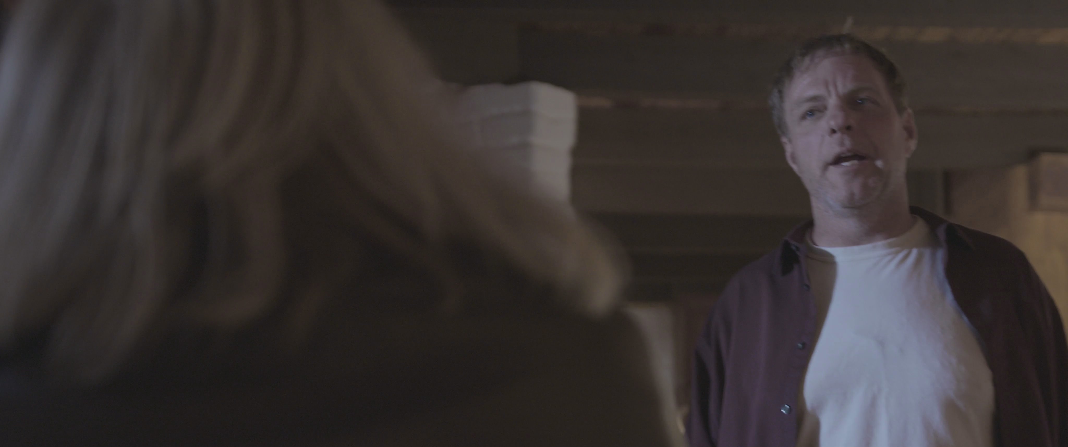 A man and a woman engage in a tense domestic interaction within a living room setting, transitioning from movement to a direct verbal exchange.