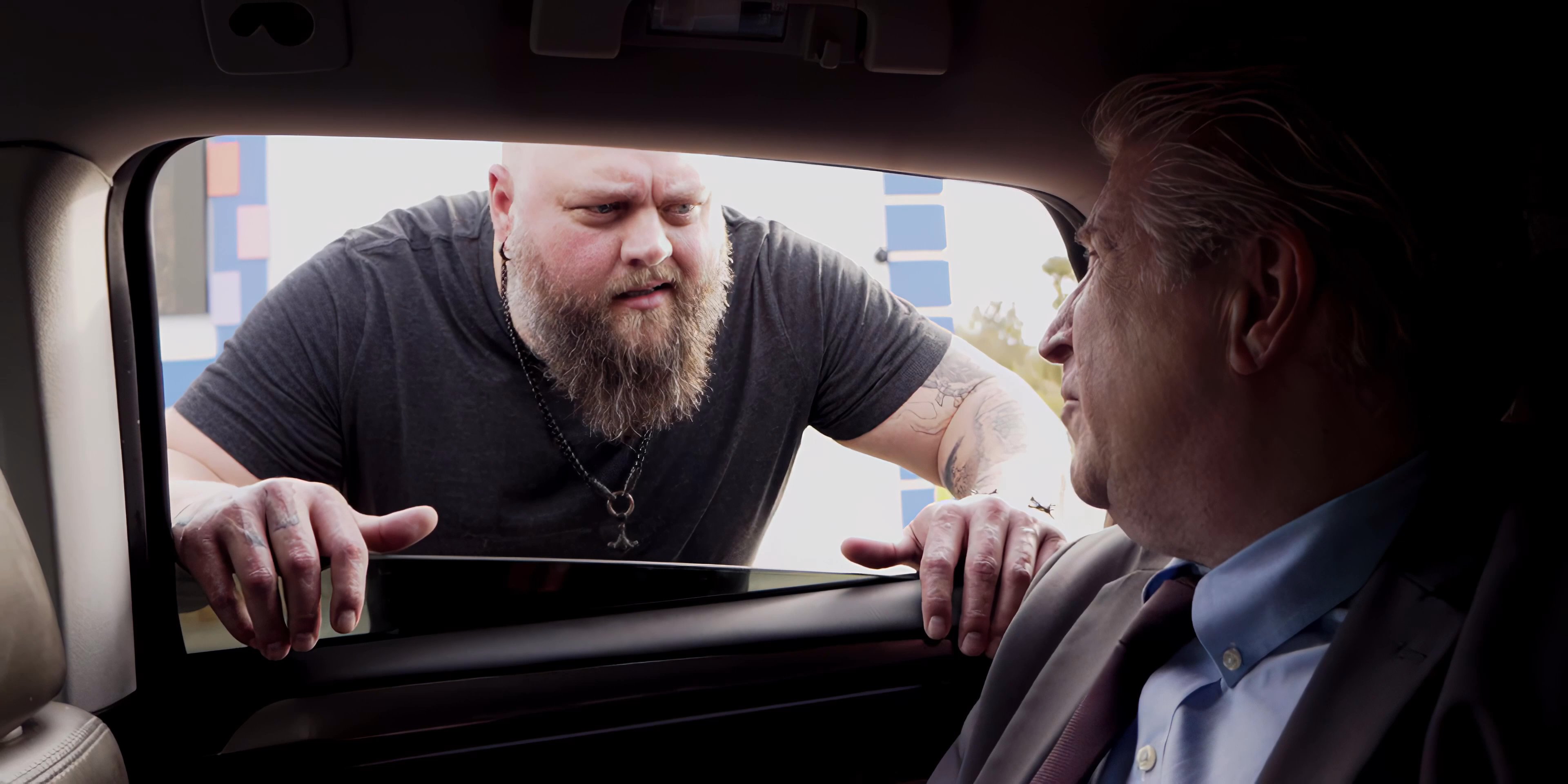 Action Bronson approaches an older man seated in the back of a luxury vehicle to engage in a direct, face-to-face conversation. The interaction involves an exchange of items, reflecting a business-like or transactional encounter.
