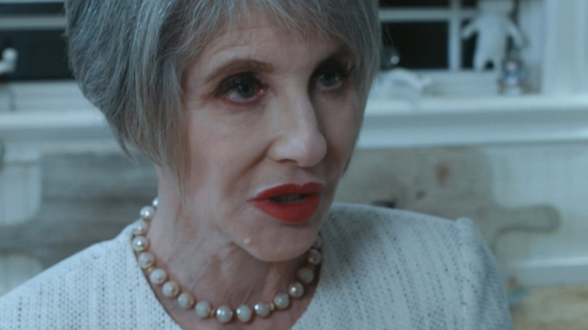 An older woman and a younger man engage in a tense conversation in a kitchen before the man retreats to his vehicle to speak with another man through the window.
